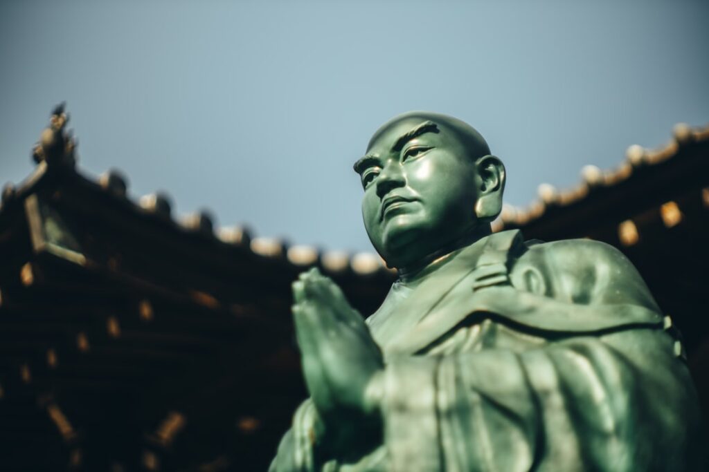 寺院前的僧人铜像，呼应玄奘西行、出境与唐代路引制度。摄影：Hongwei FAN / Unsplash